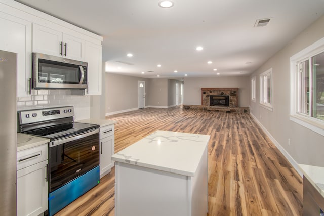 kitchen with wood-type flooring, white cabinetry, backsplash, and appliances with stainless steel finishes