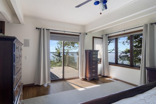 unfurnished bedroom with ceiling fan, a water view, dark wood-type flooring, and multiple windows