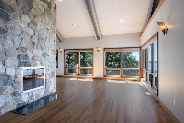 unfurnished living room with beamed ceiling, a stone fireplace, and hardwood / wood-style floors