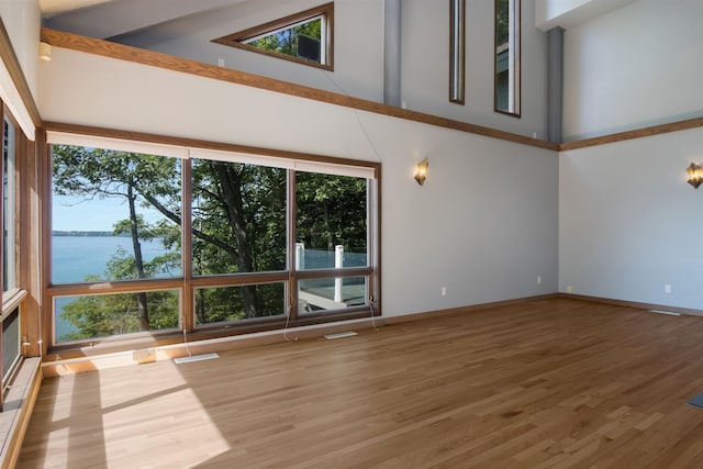 unfurnished living room featuring beamed ceiling, a water view, a healthy amount of sunlight, and high vaulted ceiling