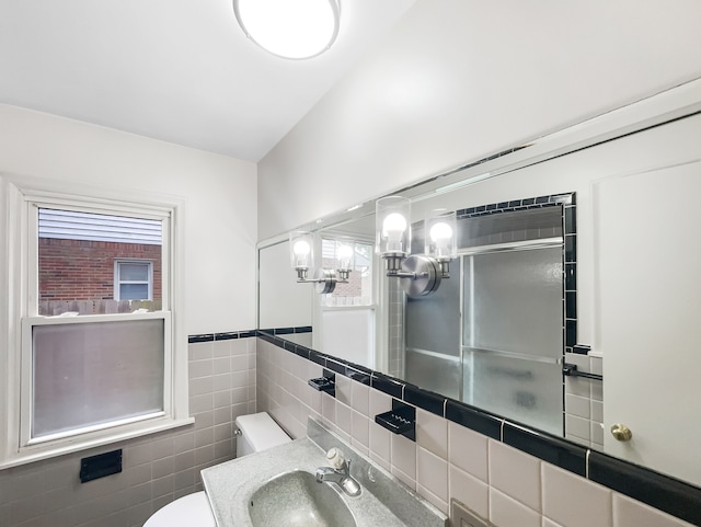 bathroom with sink, a shower with door, tile walls, and toilet