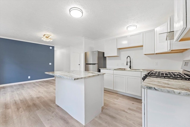 kitchen featuring stainless steel refrigerator, white cabinetry, sink, and a center island