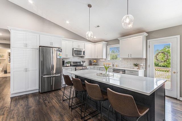 kitchen featuring white cabinets, stainless steel appliances, vaulted ceiling, and hanging light fixtures