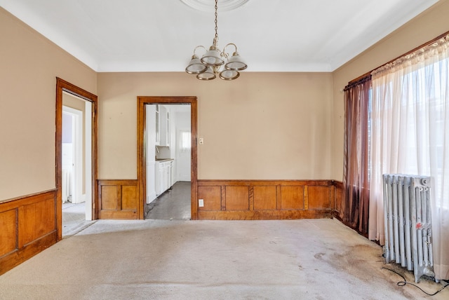 spare room featuring an inviting chandelier, radiator, and wood walls