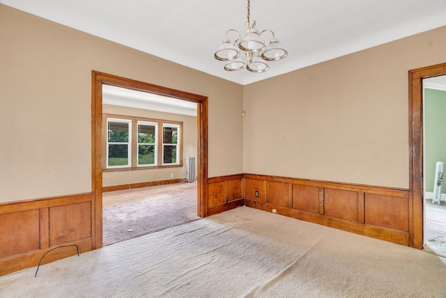 carpeted empty room with radiator, wooden walls, and a chandelier