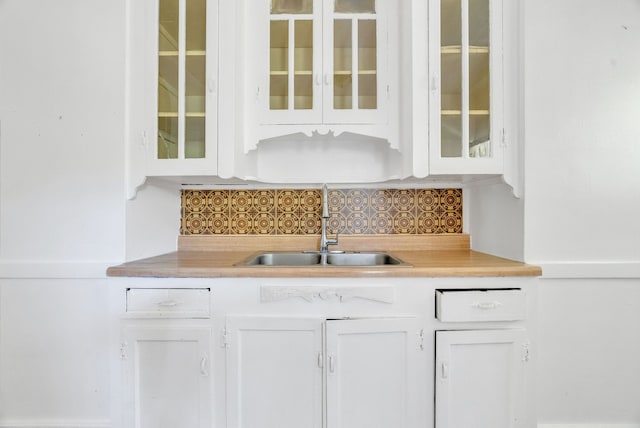 bar with decorative backsplash, white cabinetry, and sink