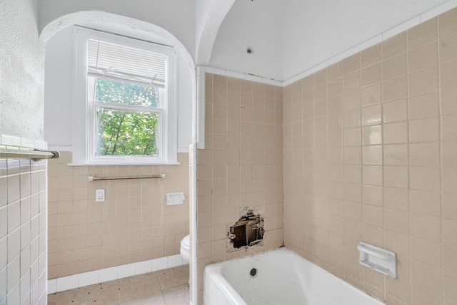 bathroom featuring toilet, tile patterned flooring, tile walls, and a washtub