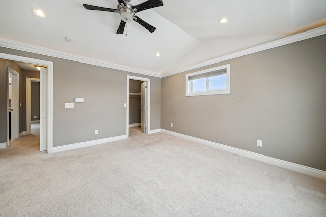 unfurnished bedroom featuring ceiling fan, crown molding, lofted ceiling, a walk in closet, and light carpet