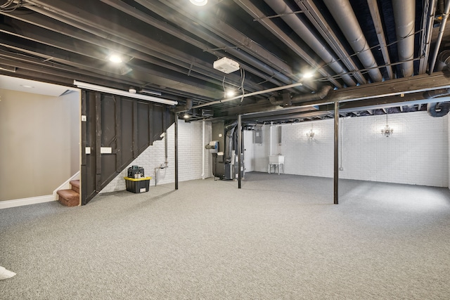 basement featuring sink, carpet floors, heating unit, and brick wall