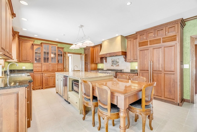 kitchen featuring sink, decorative light fixtures, dark stone countertops, custom exhaust hood, and a center island with sink