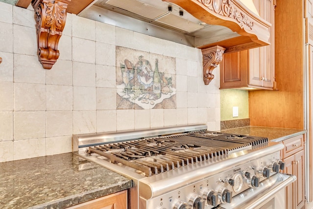 kitchen with high end stainless steel range, dark stone counters, ventilation hood, and tasteful backsplash