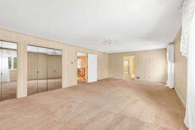 unfurnished bedroom with light colored carpet, ceiling fan, and multiple closets