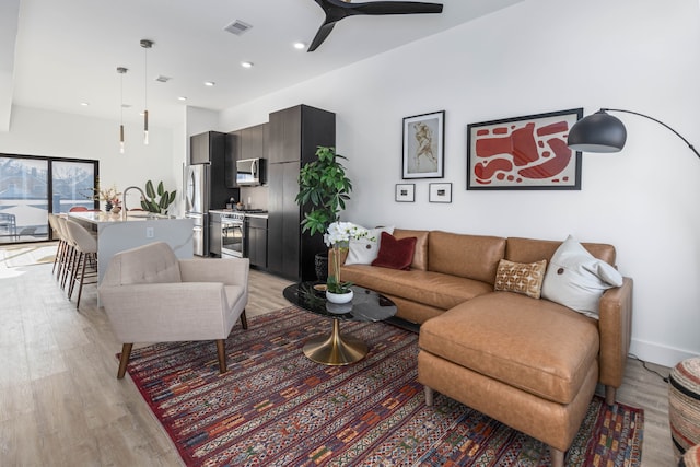 living room featuring light hardwood / wood-style flooring, ceiling fan, beverage cooler, and sink