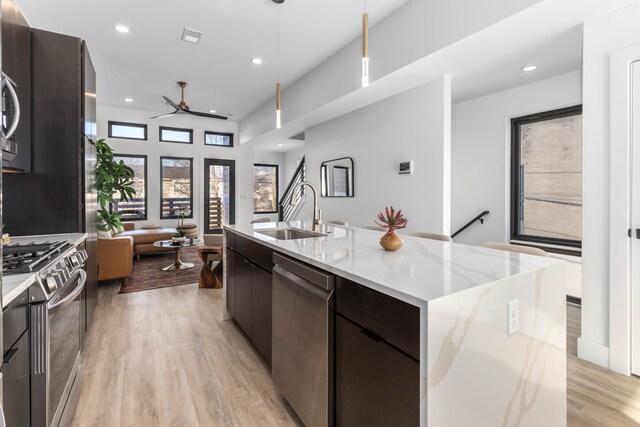 kitchen featuring a kitchen island with sink, sink, light wood-type flooring, decorative light fixtures, and stainless steel appliances