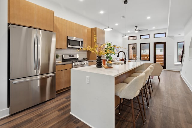 kitchen featuring sink, a breakfast bar area, hanging light fixtures, stainless steel appliances, and an island with sink