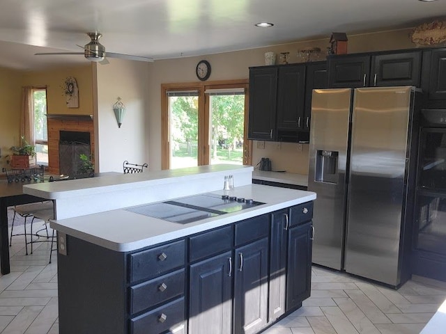 kitchen featuring stainless steel fridge, black electric stovetop, blue cabinets, ceiling fan, and a center island