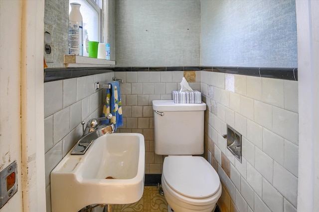 bathroom with toilet, tile walls, and sink