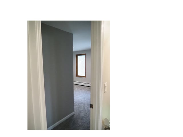 hallway with dark colored carpet and a baseboard radiator