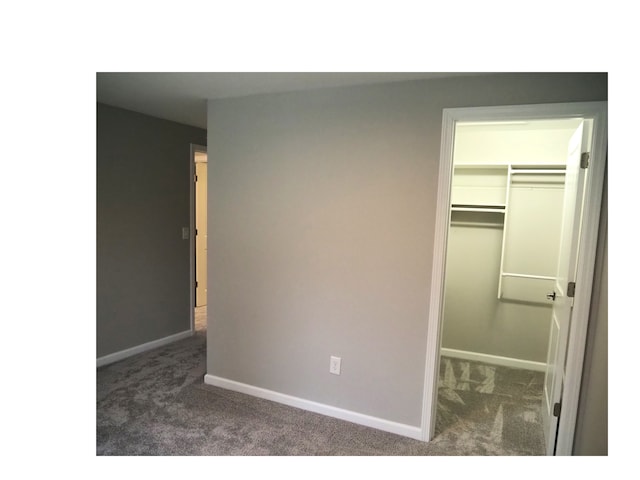 unfurnished bedroom with a walk in closet, dark carpet, and a closet