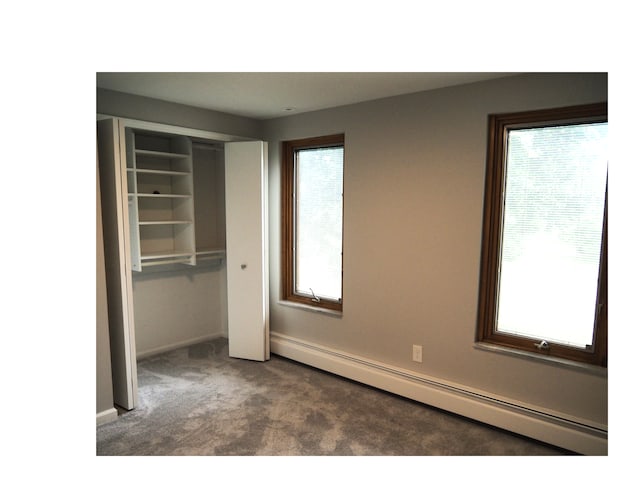 unfurnished bedroom with baseboard heating, multiple windows, a closet, and dark carpet