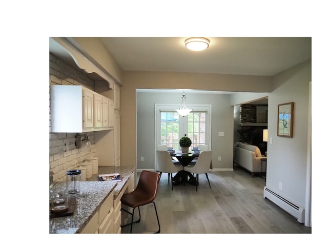 kitchen with a kitchen breakfast bar, light hardwood / wood-style flooring, light stone countertops, baseboard heating, and decorative light fixtures