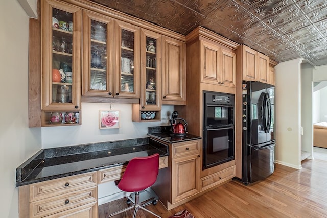 kitchen with black appliances, dark stone countertops, light hardwood / wood-style flooring, and built in desk