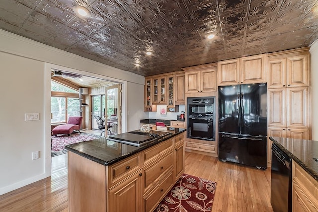 kitchen with dark stone countertops, a center island, black appliances, and light wood-type flooring