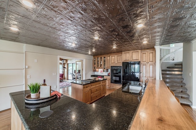 kitchen featuring black appliances, sink, light hardwood / wood-style flooring, dark stone countertops, and a large island