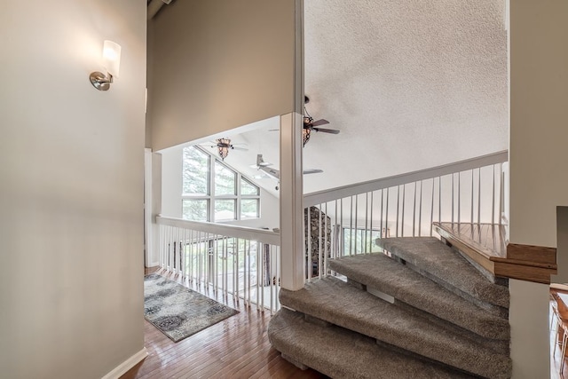 stairway featuring a high ceiling, a textured ceiling, ceiling fan, and hardwood / wood-style floors