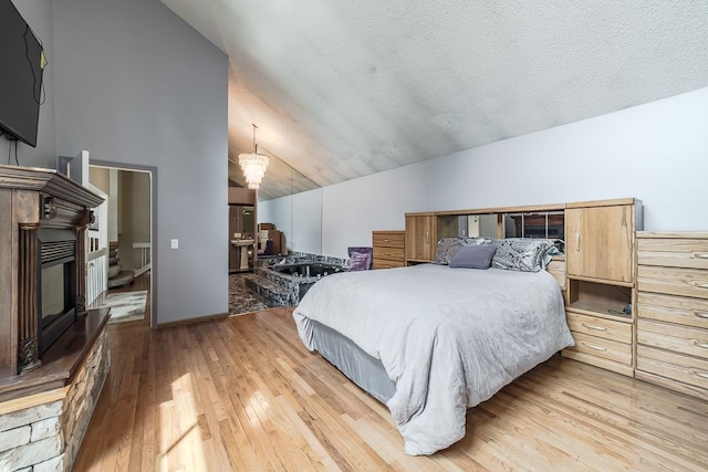 bedroom featuring a fireplace, light hardwood / wood-style floors, a textured ceiling, and vaulted ceiling