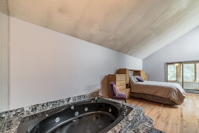 bedroom with hardwood / wood-style flooring, a textured ceiling, and vaulted ceiling