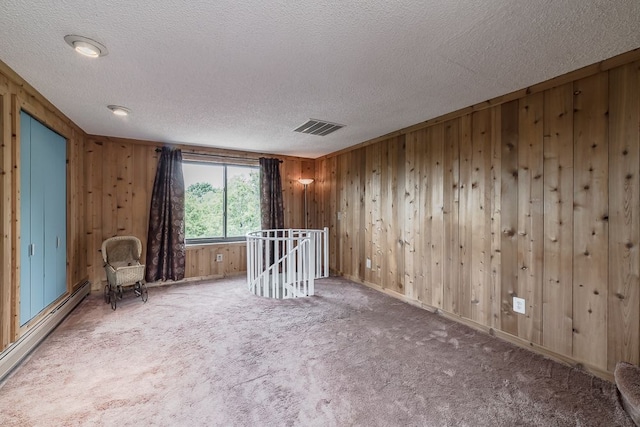 spare room featuring carpet flooring, wood walls, a textured ceiling, and a baseboard heating unit