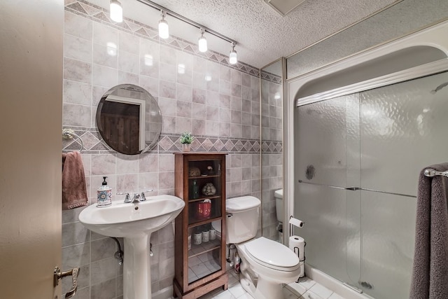 bathroom with tile patterned floors, a textured ceiling, track lighting, a shower with door, and tile walls