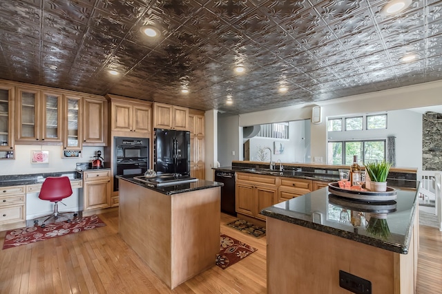 kitchen with a center island, dark stone counters, black appliances, sink, and light hardwood / wood-style floors