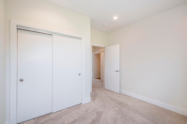 unfurnished bedroom with light colored carpet and a closet