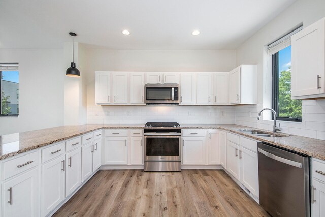 kitchen with appliances with stainless steel finishes, light wood-type flooring, sink, decorative light fixtures, and white cabinetry