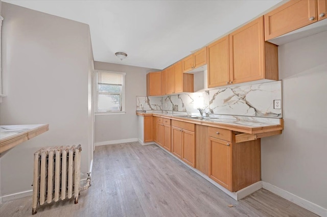 kitchen featuring tasteful backsplash, radiator heating unit, light hardwood / wood-style floors, and sink