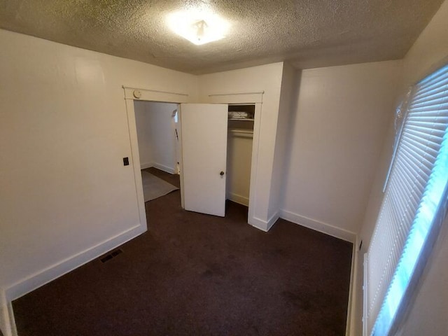 unfurnished bedroom with a closet, a textured ceiling, and dark colored carpet
