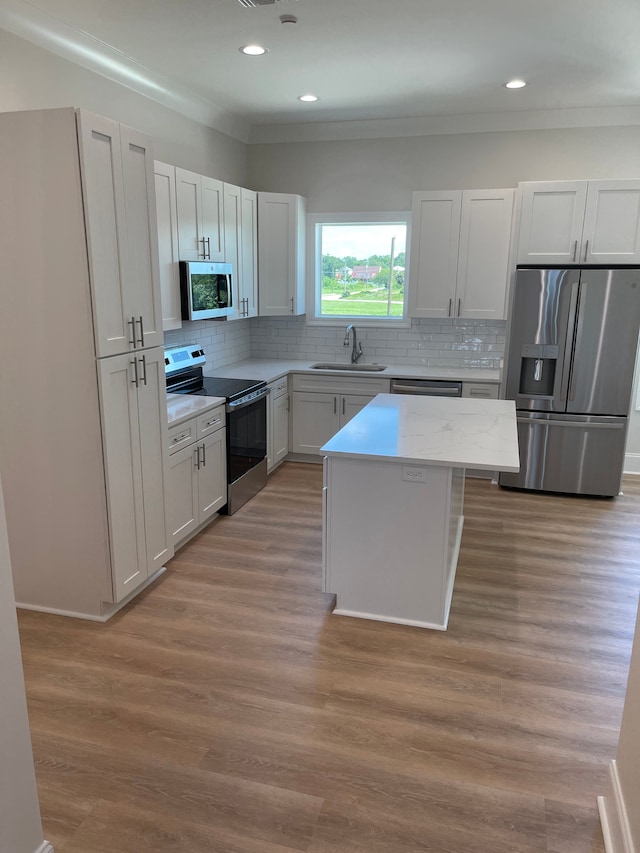 kitchen with white cabinetry, sink, stainless steel appliances, light hardwood / wood-style flooring, and a kitchen island