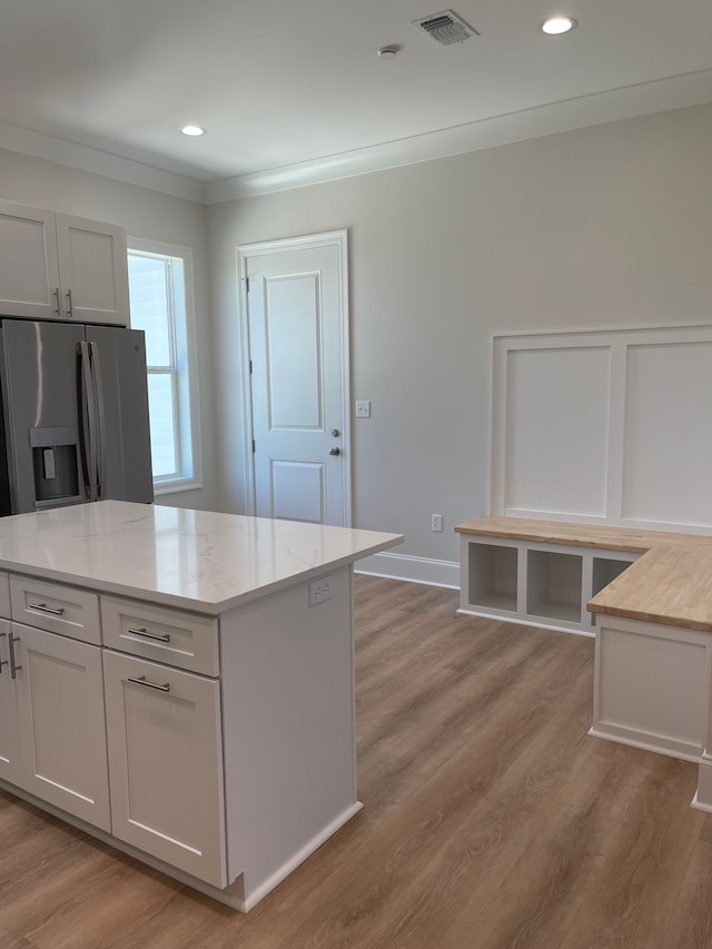 kitchen featuring crown molding, stainless steel fridge, light wood-type flooring, a kitchen island, and white cabinetry