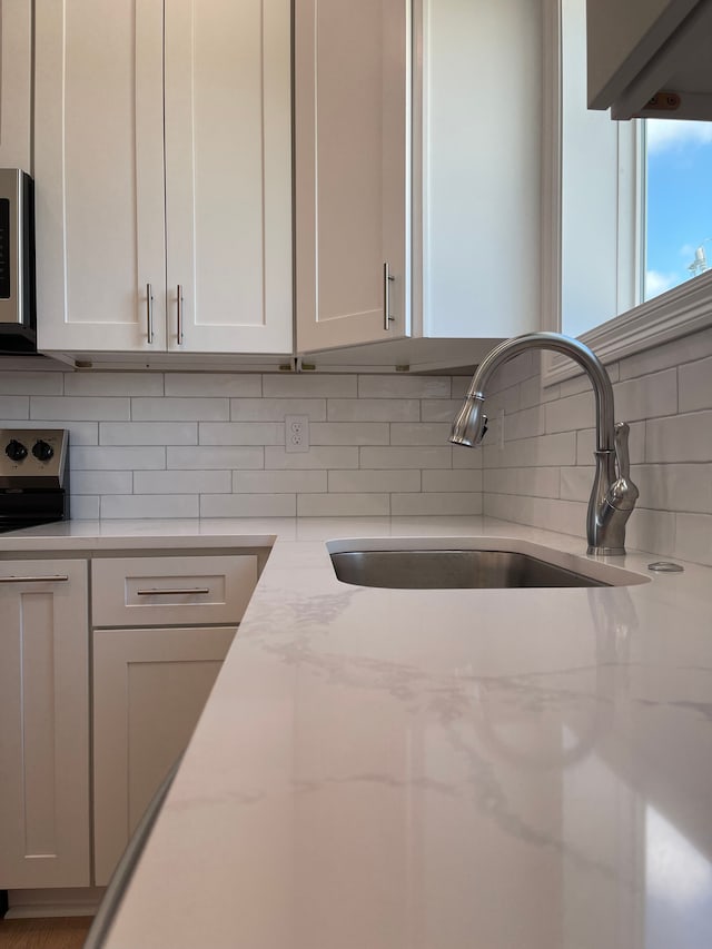 kitchen with decorative backsplash, light stone counters, sink, and white cabinets