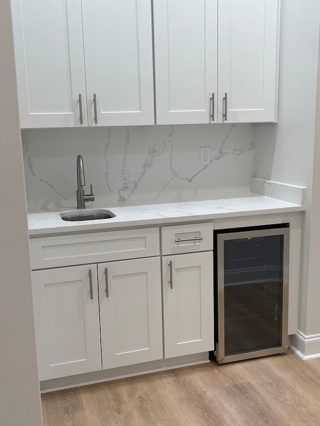 bar with light stone countertops, light wood-type flooring, beverage cooler, sink, and white cabinets