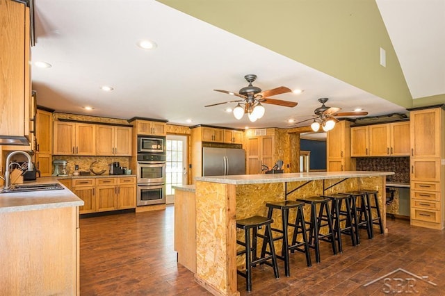 kitchen with appliances with stainless steel finishes, a kitchen breakfast bar, ceiling fan, dark wood-type flooring, and sink