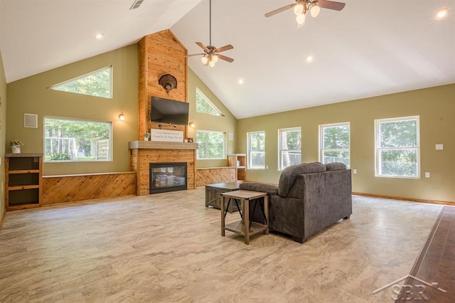 living room featuring wooden walls, ceiling fan, a fireplace, and high vaulted ceiling