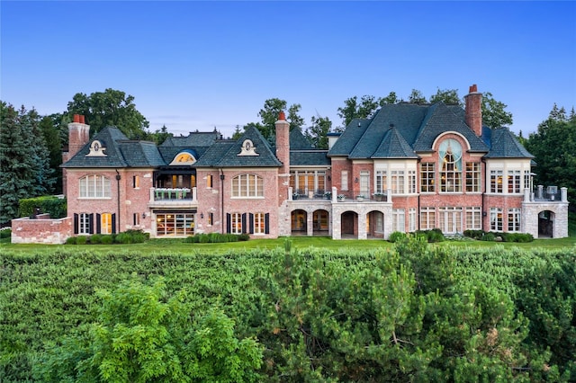back of house with brick siding, a high end roof, a balcony, and a chimney