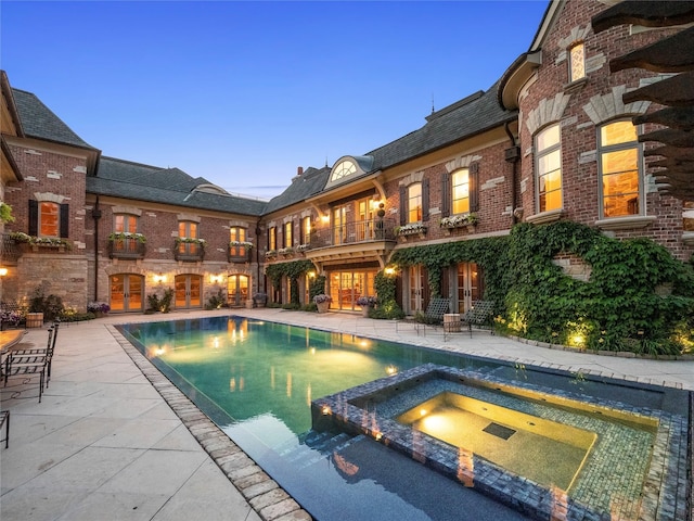 pool at dusk with an in ground hot tub and a patio