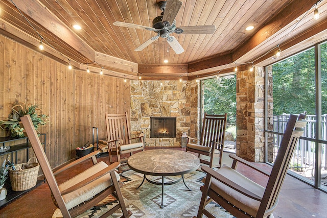 sitting room with wood walls, ceiling fan, wooden ceiling, and an outdoor stone fireplace