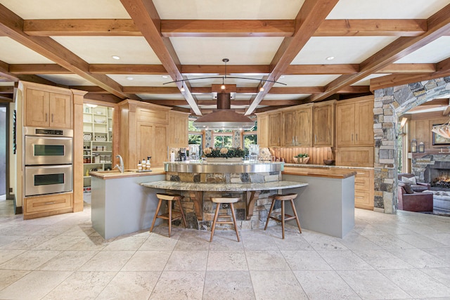 kitchen featuring coffered ceiling, a stone fireplace, beamed ceiling, double oven, and a breakfast bar area