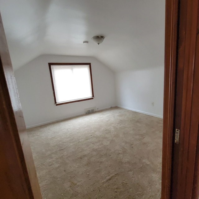 bonus room with light colored carpet and vaulted ceiling