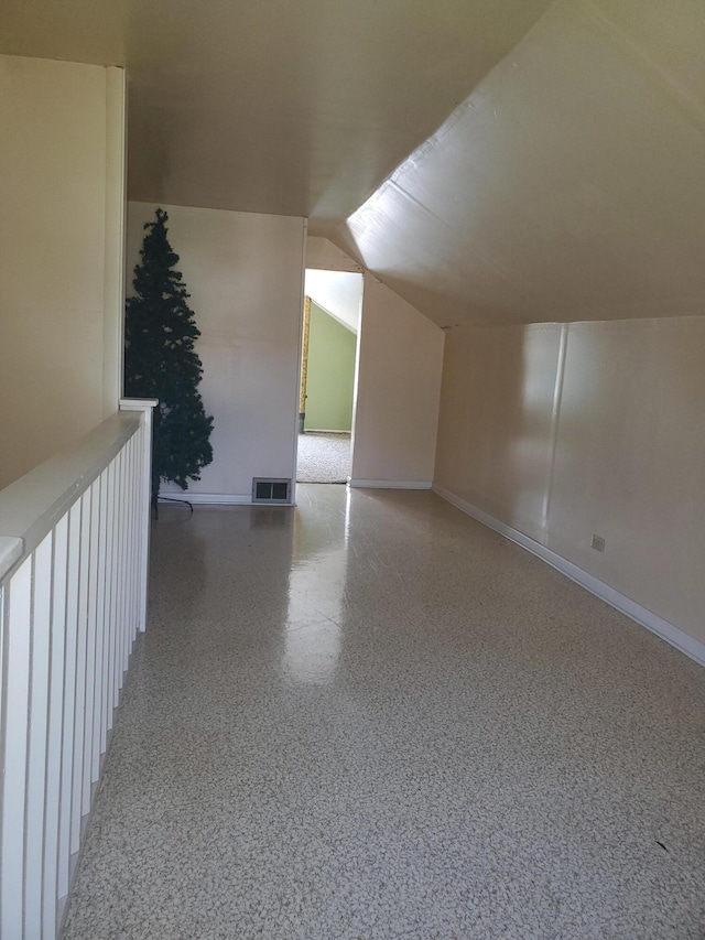 additional living space featuring vaulted ceiling, speckled floor, visible vents, and baseboards